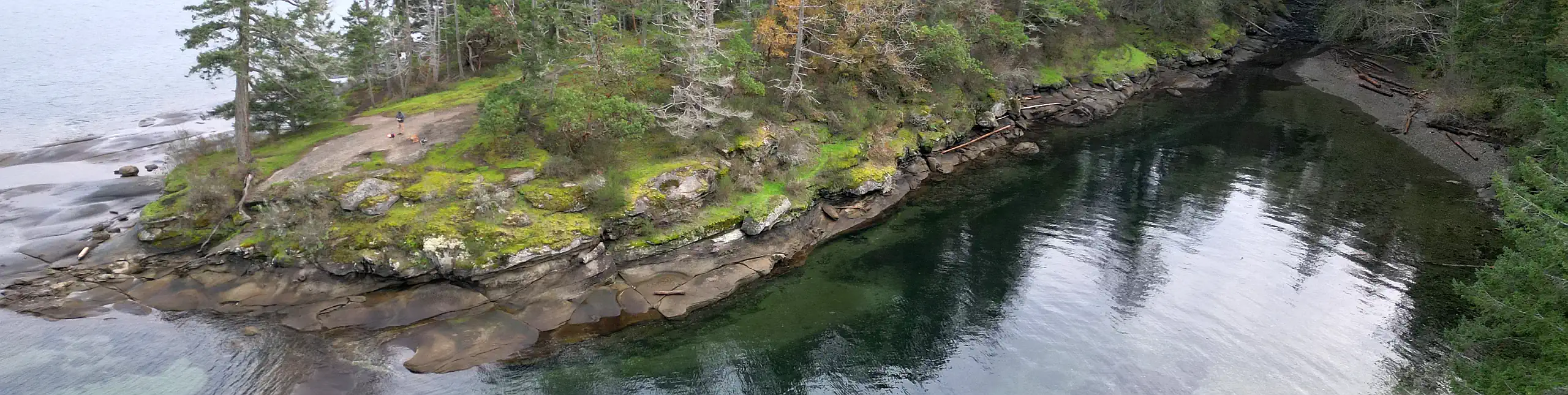 Aerial photo showing a sandstone peninsula surrounded by calm ocean waters and partly covered in forest.
