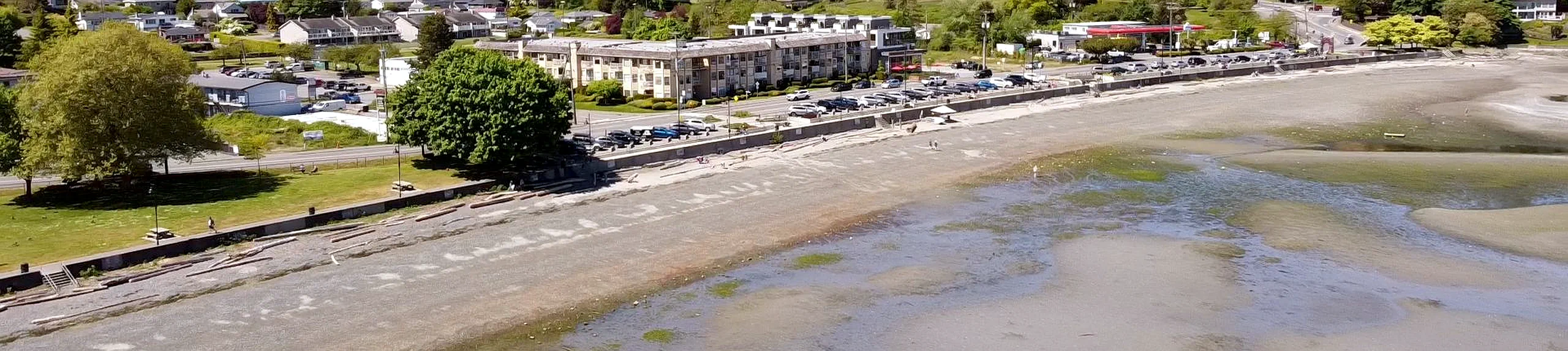 Aerial photo looking at a wide sandy beach at low tide; cars are parked above the beach.
