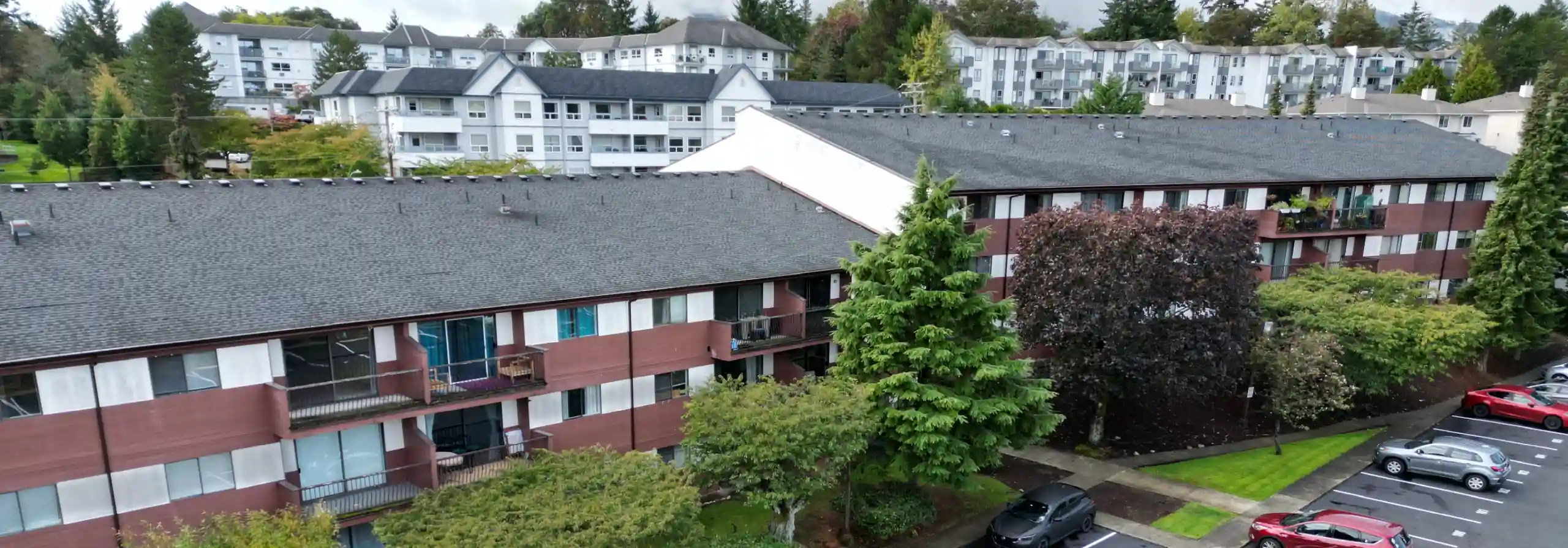 Photo showing an early 1980s low-rise apartment complex with mature landscaping; newer condo buildings rise in the near distance