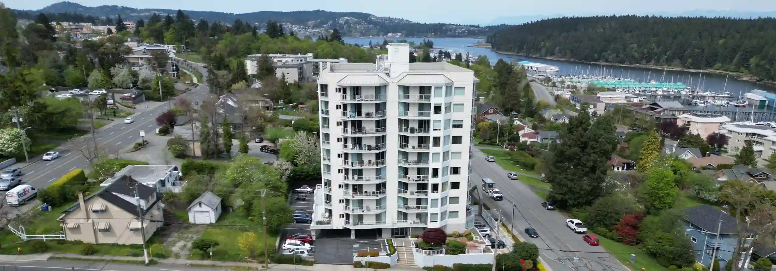 Photo of a white 1990s-era 9-storey apartment building with the blue waters of Nanaimo's Departure Bay and Newcastle Channel in the background