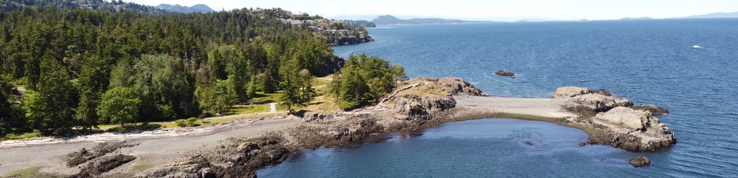 Photo showing a rocky shoreline in a park-like oceanside setting; at right a gravel 