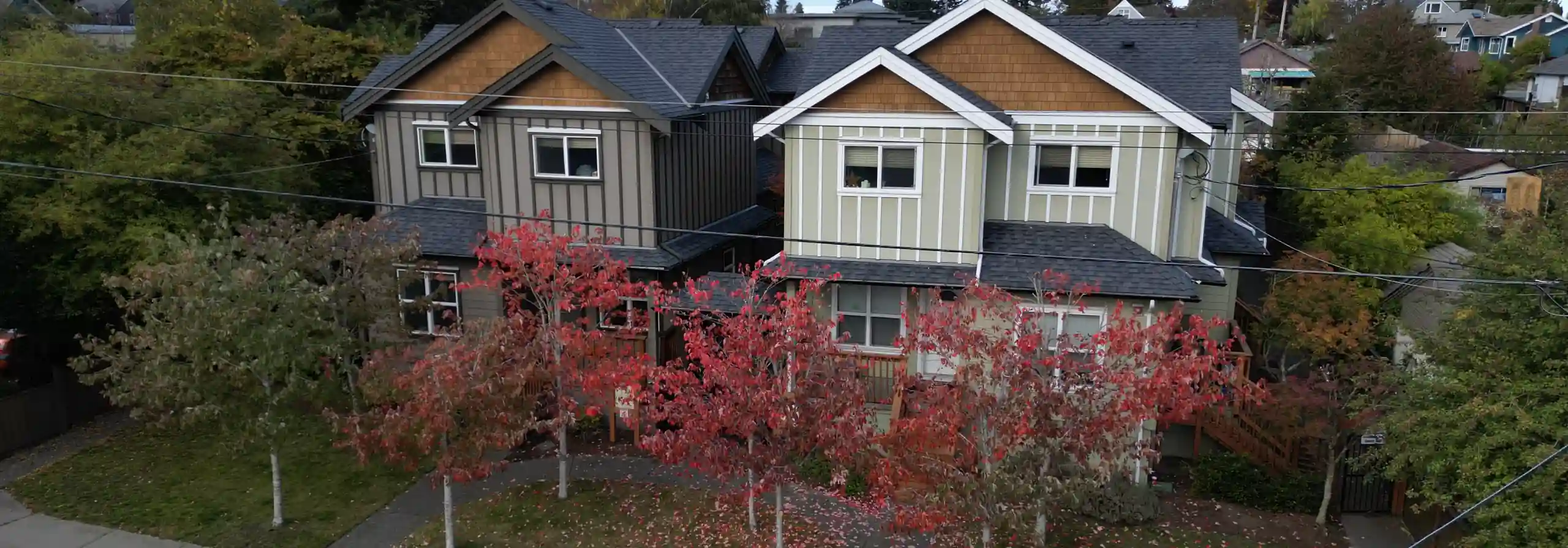 Drone photo showing two townhouse buildings with autumnal red maples out front; an elementary school is seen in the background